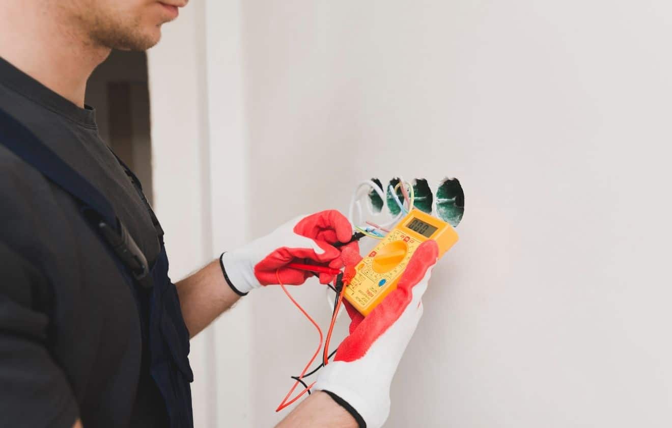 Électricien utilisant un multimètre pour diagnostiquer une panne électrique dans une habitation.