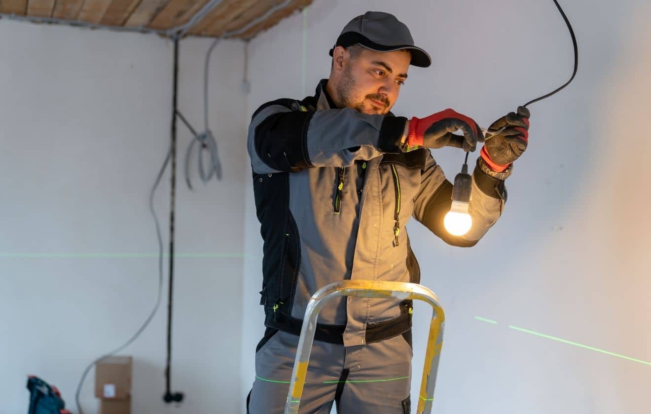 Électricien réalisant le raccordement d’un luminaire lors de travaux électriques intérieurs.
