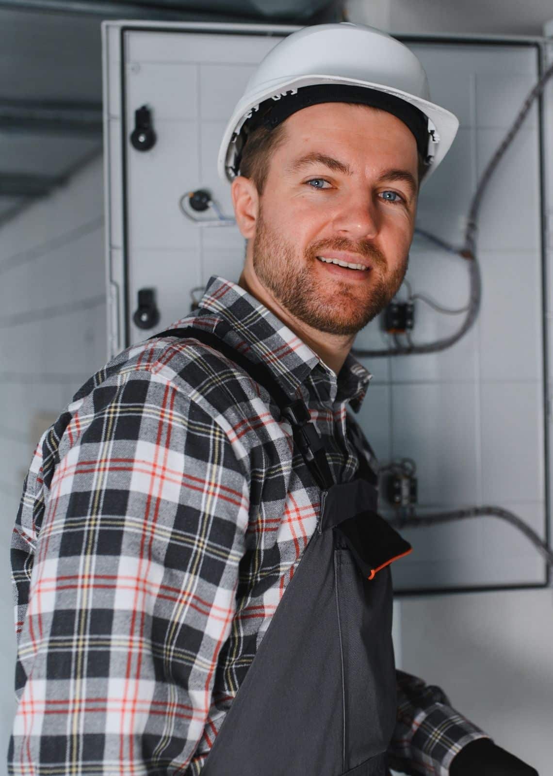 Électricien professionnel équipé d’un casque de sécurité devant un tableau électrique lors d’une intervention de contrôle et de maintenance.